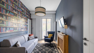 Soggiorno con divano grigio, parete libreria e poltrona blu. Ristrutturazione Trieste Roma. (Progetto Armonie)